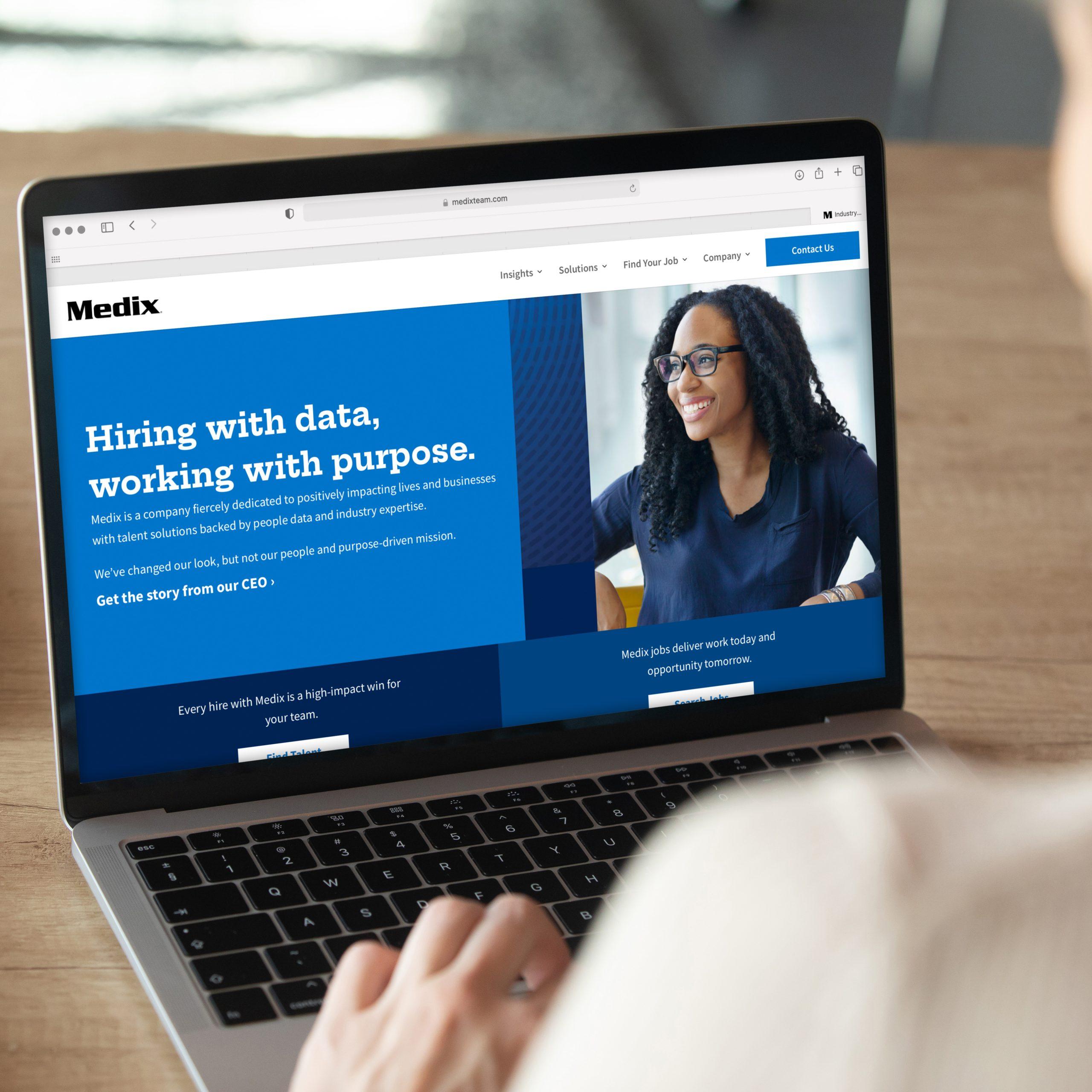 Back view of employee viewing a modern laptop featuring the Medix homepage. Page shows a happy woman, deep blue colors, and Medix's mission statement